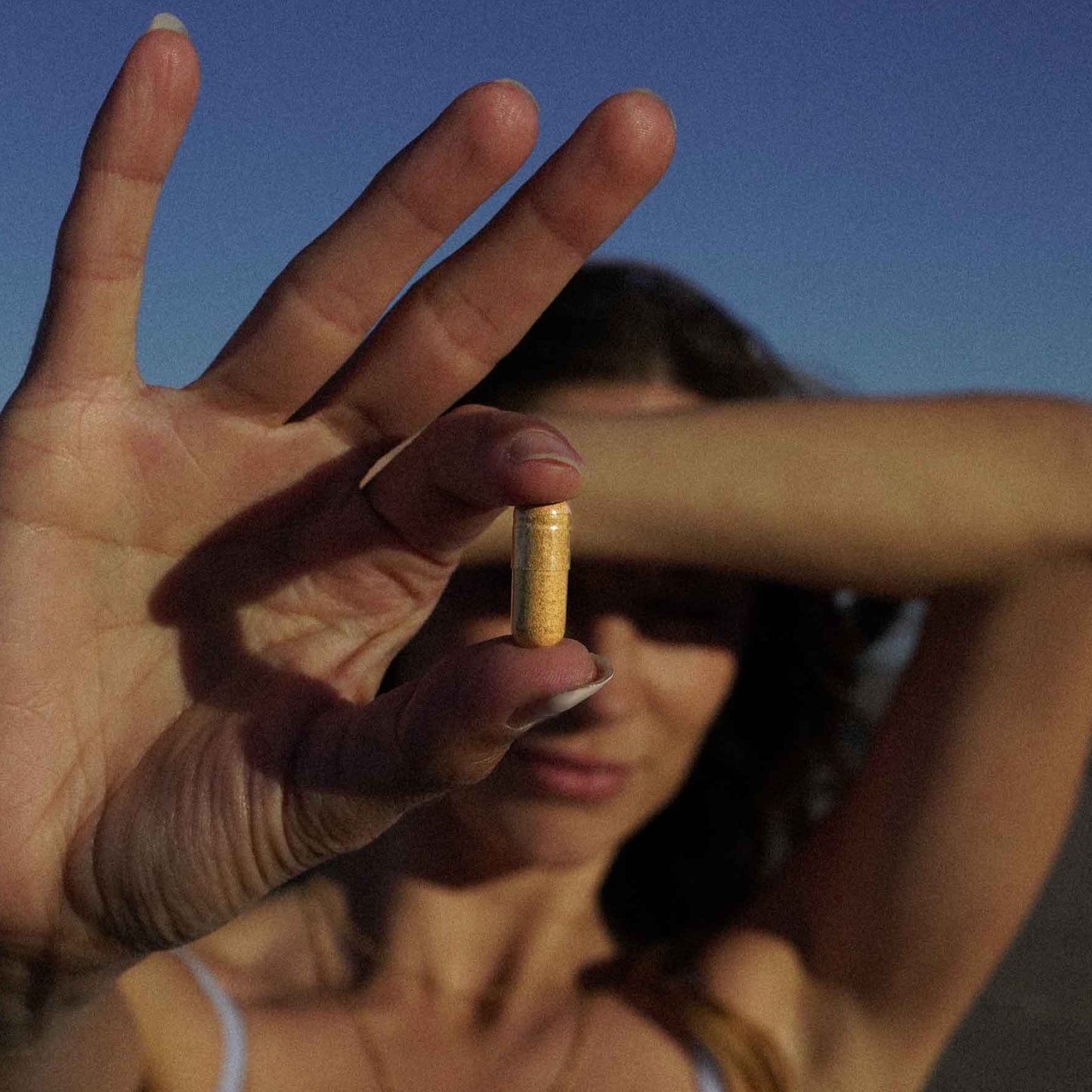 Woman on a beach holding a capsule in front of her face with a clear blue sky.